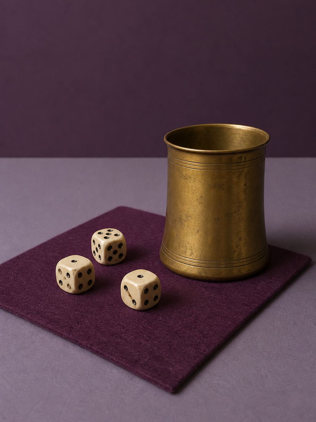 Antique ivory dice and a brass cup on a plum-felt square