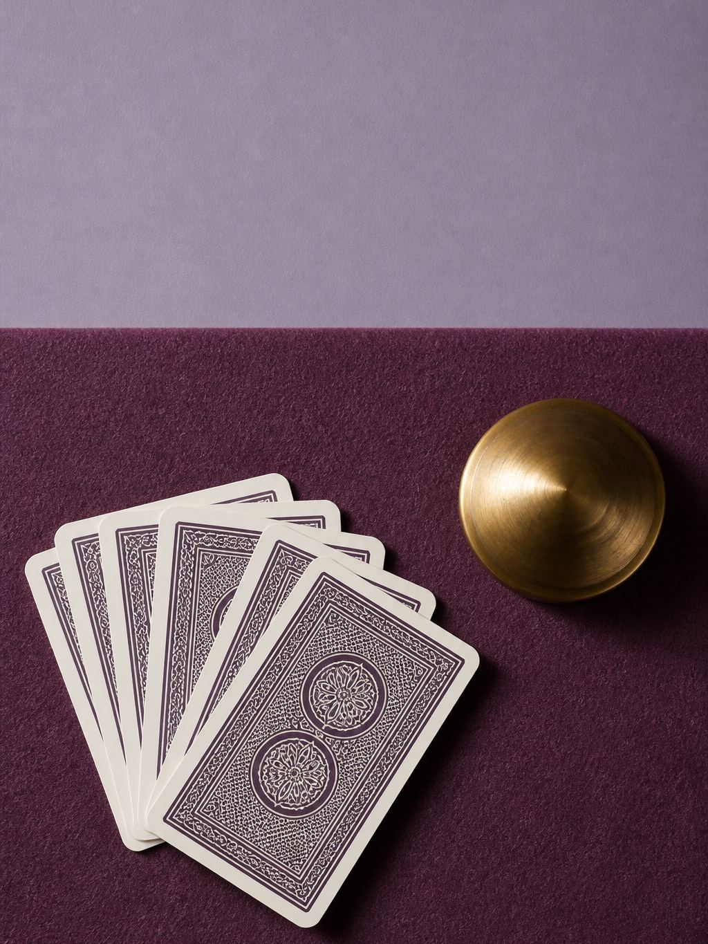 Playing cards fanned on plum felt with a brass weight