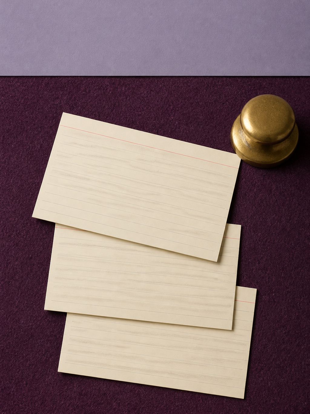 Blank index cards stacked on plum felt with a brass weight